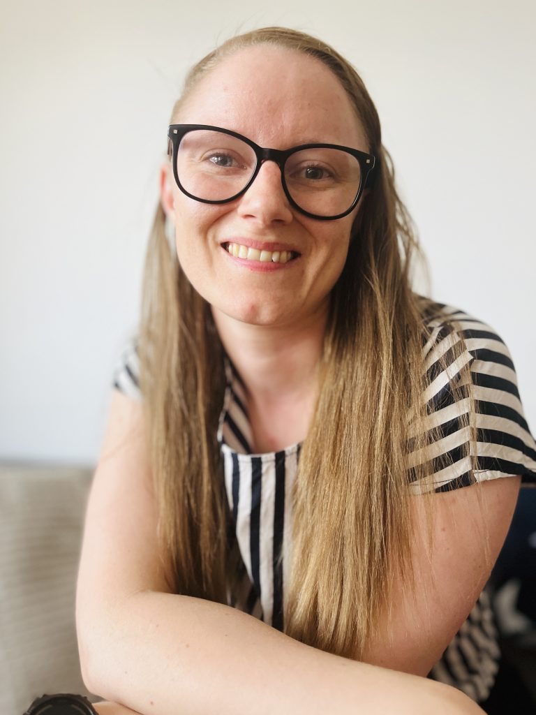 Karin Bergman frontendutvecklare, leende och avslappnad, med långt rakt hår och stora svarta glasögon, iklädd en randig svartvit tröja mot en ljus bakgrund.